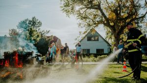A firefighter extinguishes a controlled fire as a crowd watches during a demonstration on a sunny day.