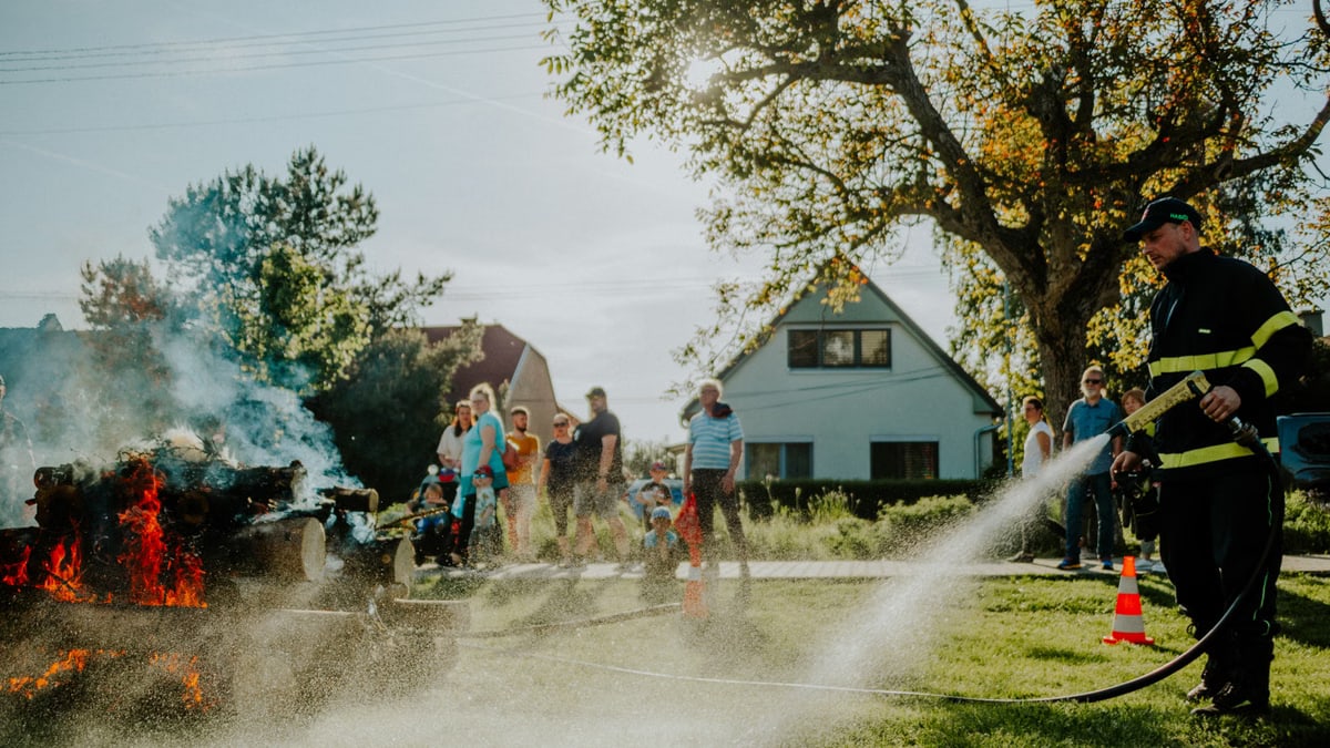 A firefighter extinguishes a controlled fire as a crowd watches during a demonstration on a sunny day.